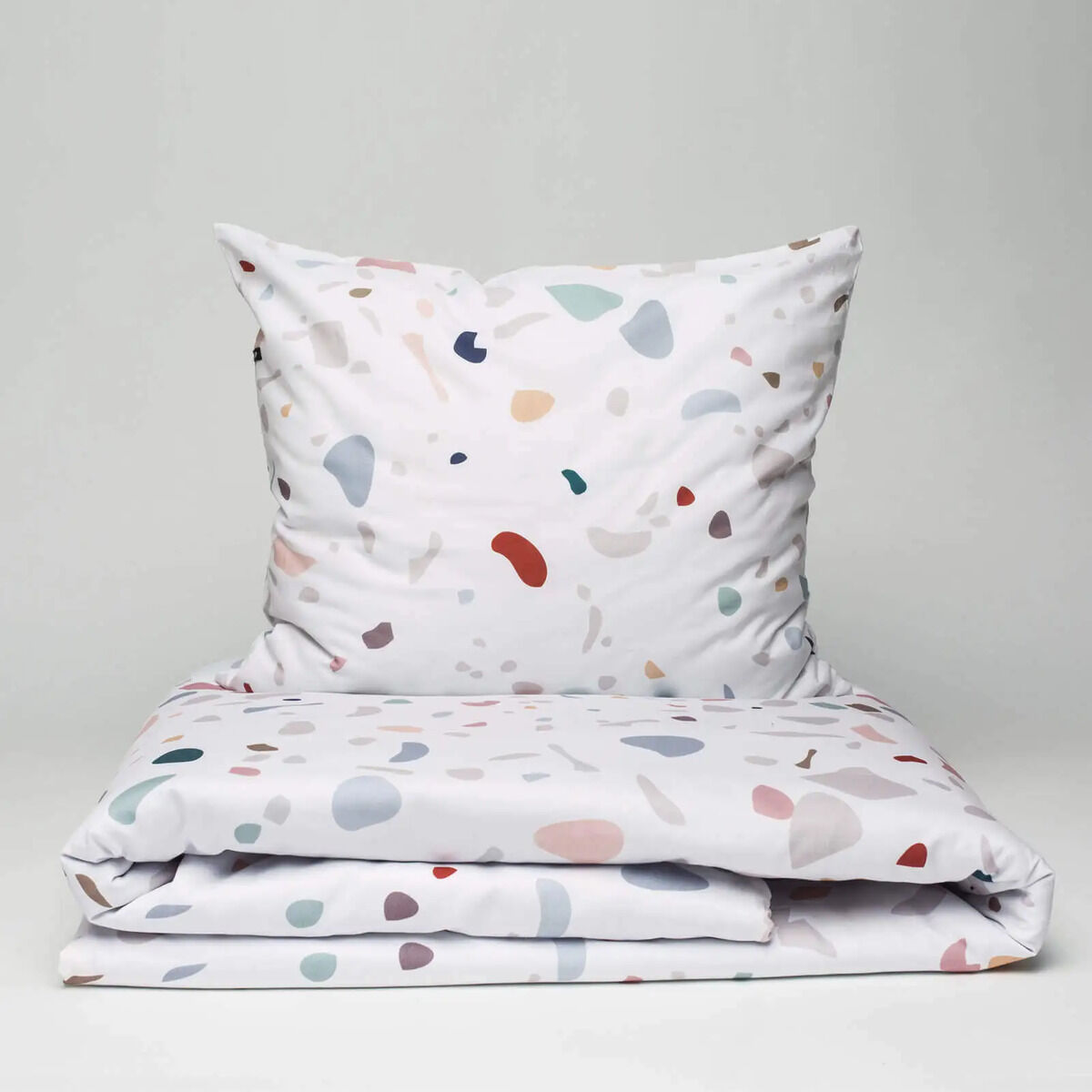 Auf dem Bild ist ein Bettwäsche-Set der Marke HOP DESIGN SP Z O O mit dem Motiv „Terrazzo“ zu sehen. Das Set besteht aus einem Bettbezug und einem Kopfkissenbezug in Weiß mit bunten, organischen Farbsprenkeln in Pastelltönen. Der Hintergrund ist schlicht hellgrau gehalten.
