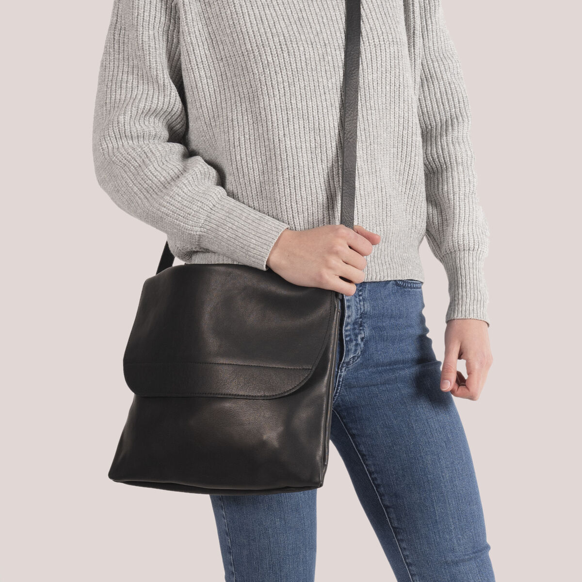 Person trägt eine schwarze Ledertasche namens »ZEIT Messengerbag« über der Schulter. Die Person trägt einen grauen Pullover und eine blaue Jeans.