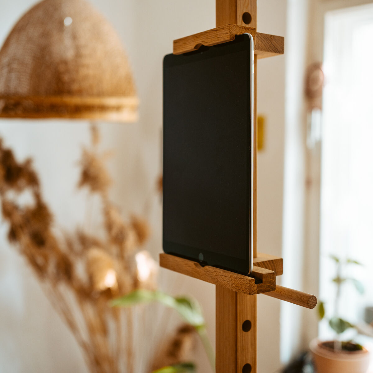 Mobiles Device Stativ "ERA" von Frau Caze aus Eiche natur und Birkensperrholz. Ein Tablet ist eingespannt; der Ständer steht in einem modern eingerichteten Raum mit Naturdeko, Pflanzen und warmem Licht. Das Design ist geradlinig und funktional.