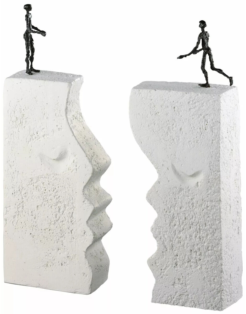 Eine abstrakte Skulptur bestehend aus zwei weißen, grob strukturierten Blöcken in Form menschlicher Gesichter, mit kleinen menschlichen Figuren aus Metall darauf platzierend, die sich zueinander hinbewegen.
