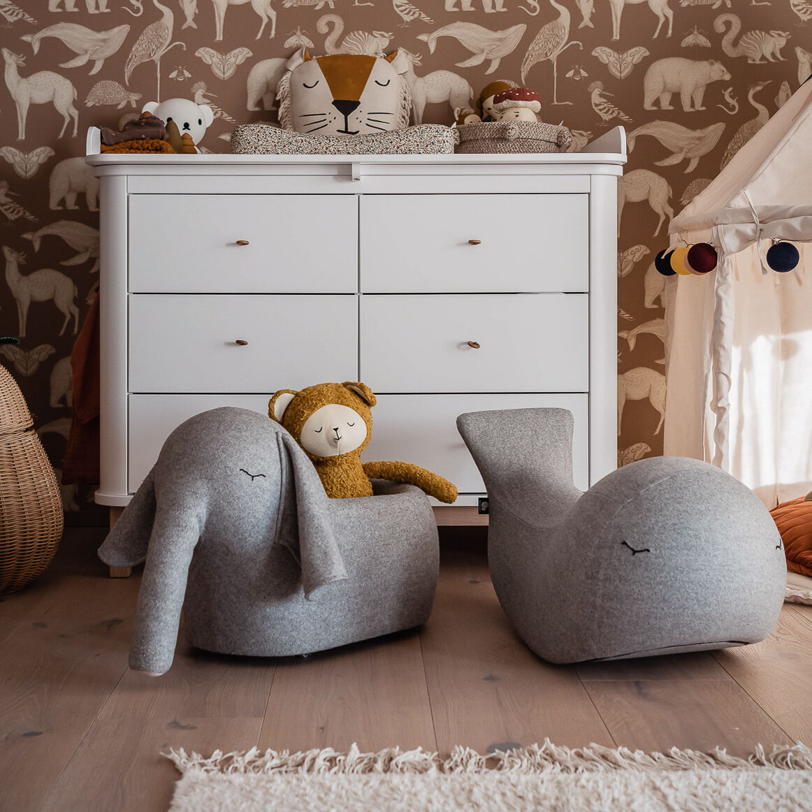 Kinderzimmer mit weißen Möbeln und Tierfiguren. Ein grauer Schaukelwal und ein grauer Schaukelelefant auf dem Boden. Plüschtiere und Dekoration im Safari-Thema im Hintergrund.
