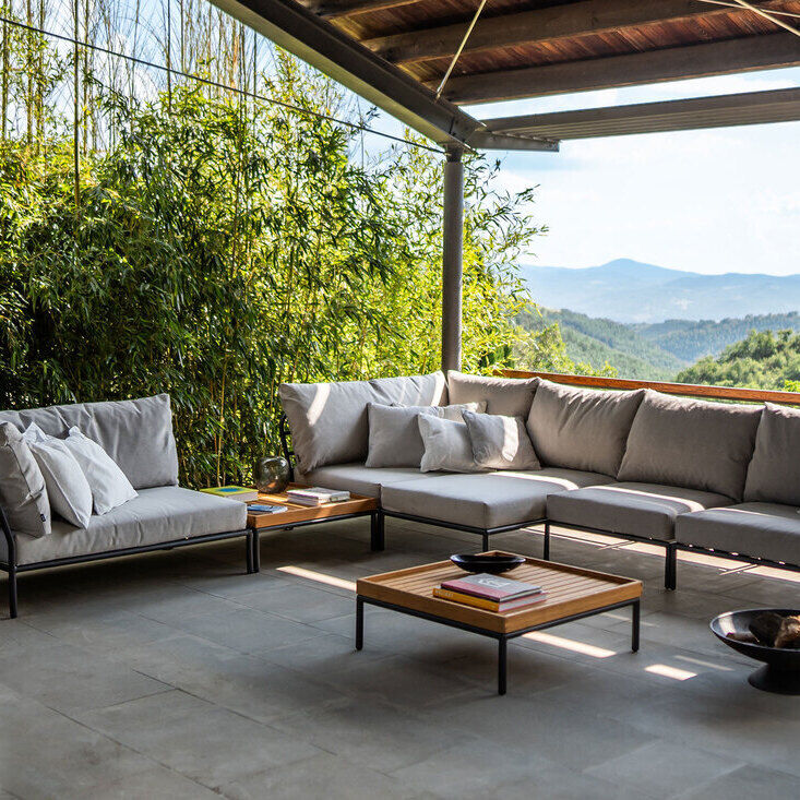 Ein moderner Loungesessel und Couchtische der Marke »LEVEL 2« auf einer Terrasse mit grauen Kissen und mit Blick auf die grünen Hügel und Berge im Hintergrund.