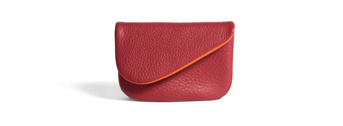 Ein kleines, rotes Schlüsseletui aus Leder mit einer orangefarbenen Naht, auf weißem Hintergrund.