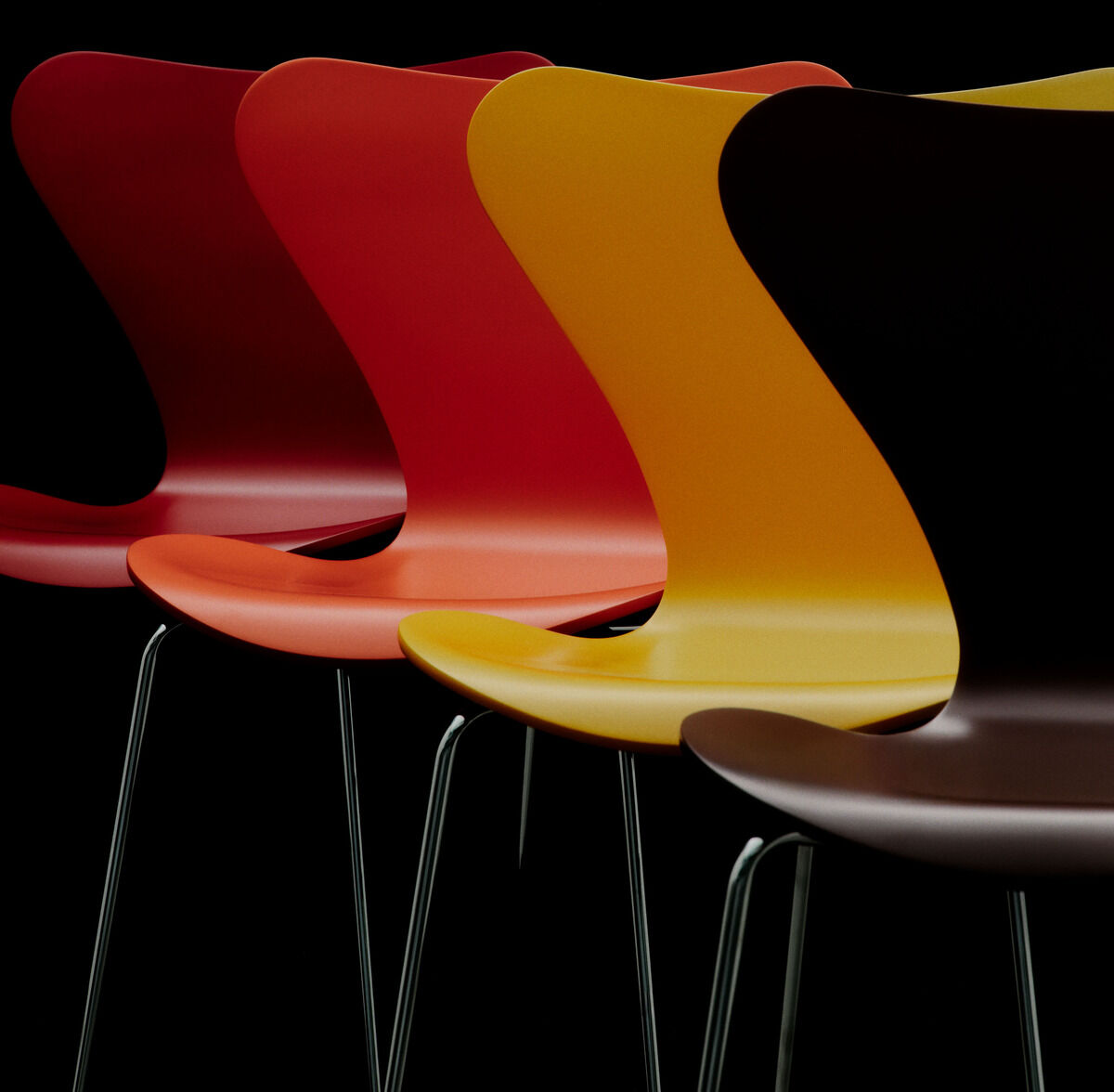 Vier Stühle der Serie 7, Edition Verner Panton von Fritz Hansen, stehen seitlich versetzt nebeneinander. Die ikonischen Schalen in Braun, Gelb, Rot und Orange sind aus lackiertem Buchenfurnier und haben ein filigranes Stahlrohrgestell vor schwarzem Hintergrund.