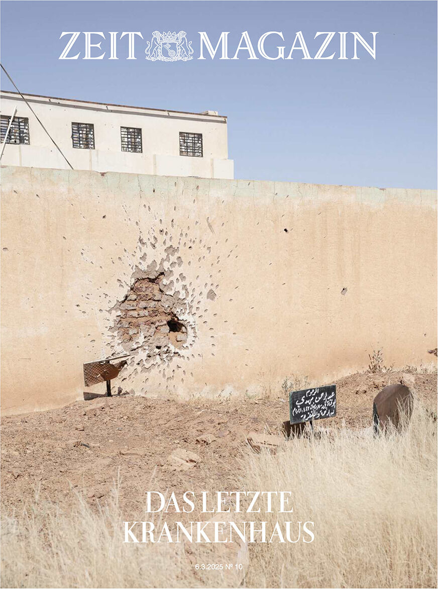 Titelseite des ZEIT Magazins mit der Überschrift 'Das letzte Krankenhaus'. Die Abbildung zeigt eine beschädigte Mauer mit einem großen Einschussloch, das auf ein Krisengebiet hinweist. Im Hintergrund ist ein Gebäude zu sehen, während der Vordergrund trockenes Gras und Schilder zeigt. Minimalistische Farbpalette in Beige und Braun.