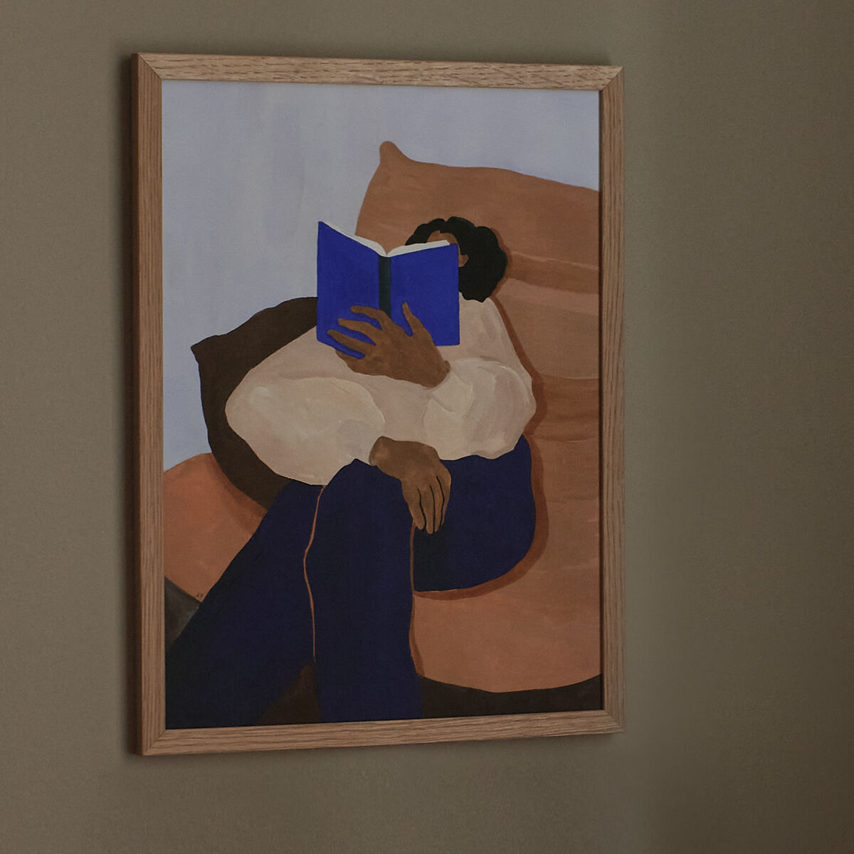 Ein gerahmtes Kunstwerk von Hanna Peterson mit dem Titel 'The Togo'. Das Bild zeigt eine abstrakte Darstellung einer sitzenden Person, die ein Buch liest. Die Farben des Bildes sind hauptsächlich Beige, Braun und Blau, passend zu einer schlichten, modernen Einrichtung.