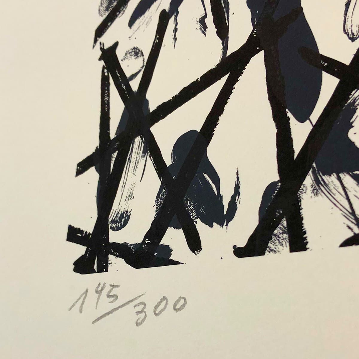 Das Bild zeigt einen Druckgrafik von Günther Uecker mit dem Titel »Verbindungen – Verletzungen«. Es handelt sich hierbei um eine abstrakte, begrenzt aufgelegte Edition, die in Schwarz-Weiß-Grau-Tönen gestaltet ist. Auf dem Bild sind Unterschrift und Nummerierung (145/300) zu erkennen.