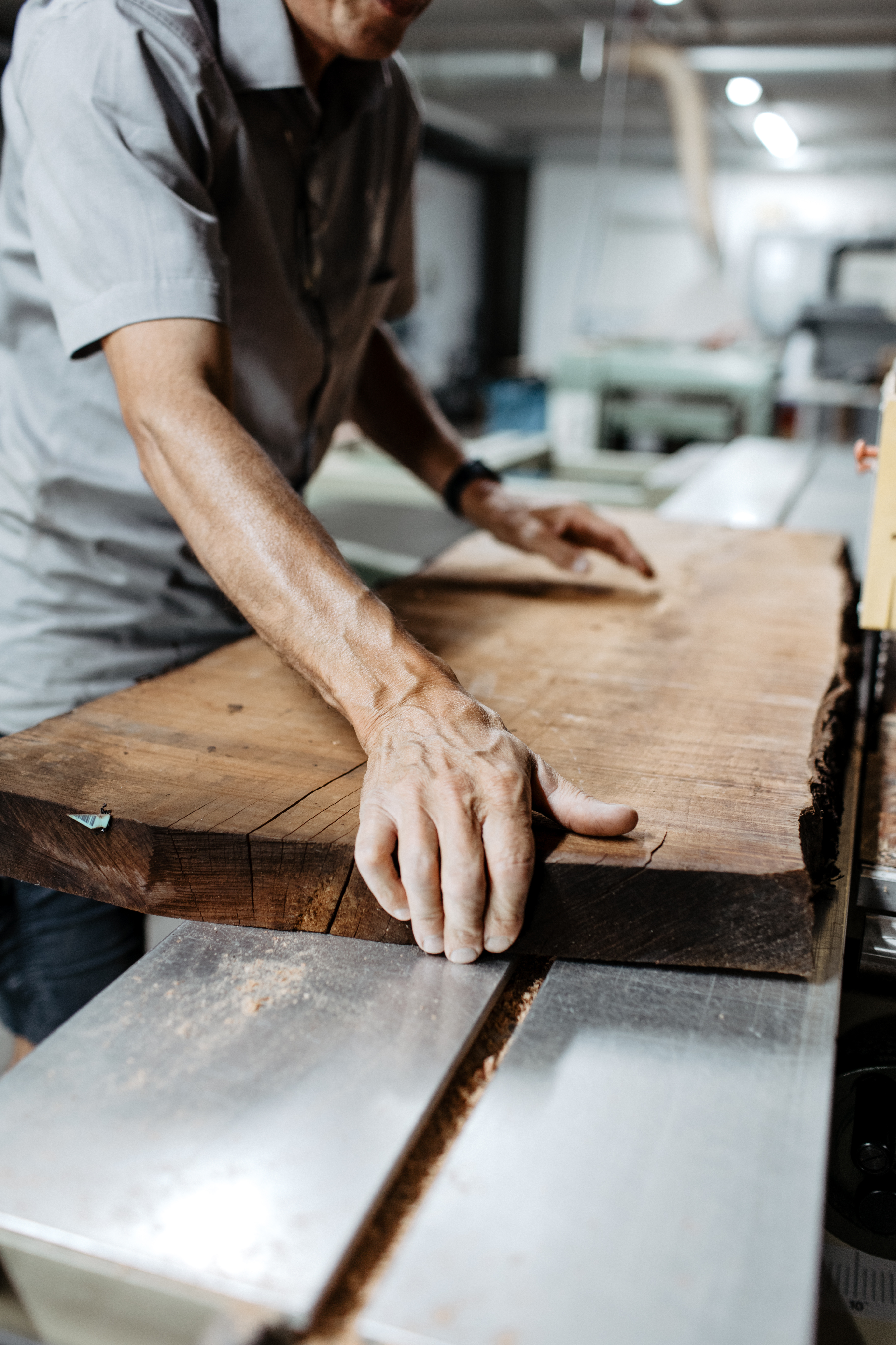Hand eines Mannes führt ein großes Holzbrett durch eine Tischkreissäge in einer Werkstatt