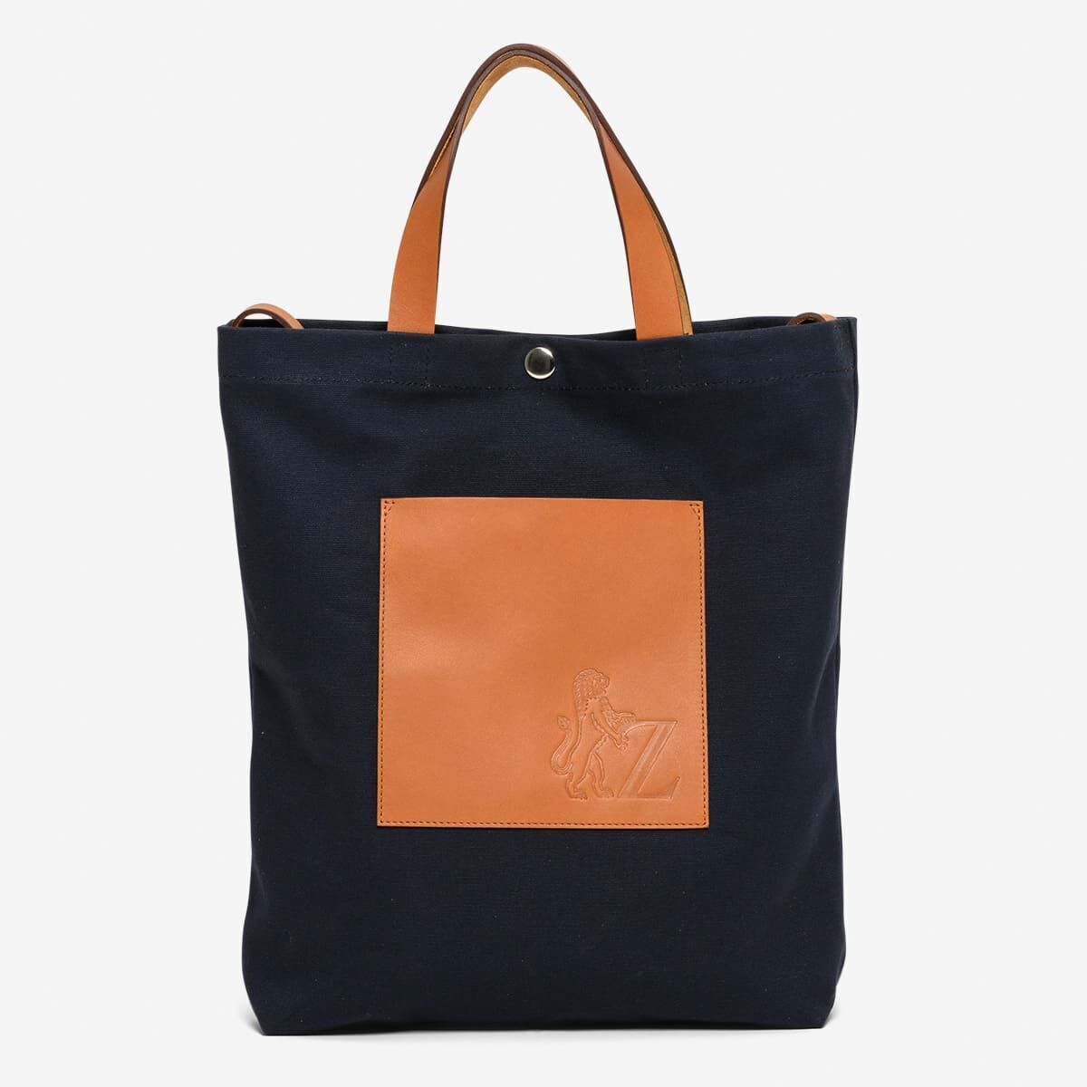 Schwarze Einkaufstasche aus Stoff mit braunen Ledergriffen und einer braunen Vordertasche mit ZEIT-Logo.