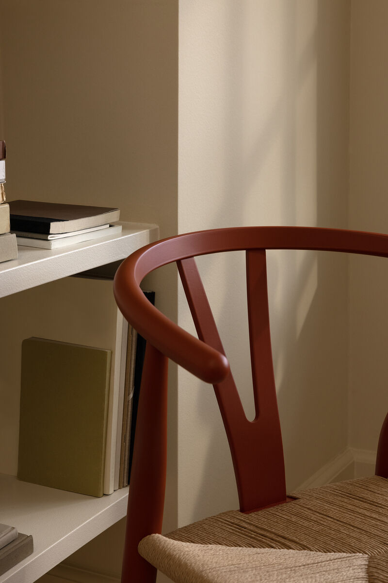 Ein CH24 Soft Stuhl von Carl Hansen in einem gemütlichen Ambiente. Der Stuhl hat ein braunes Holzgestell und eine beige, gewebte Sitzfläche. Im Hintergrund ist ein Bücherregal mit diversen Büchern zu sehen. Das Bild strahlt eine ruhige und elegante Atmosphäre aus.