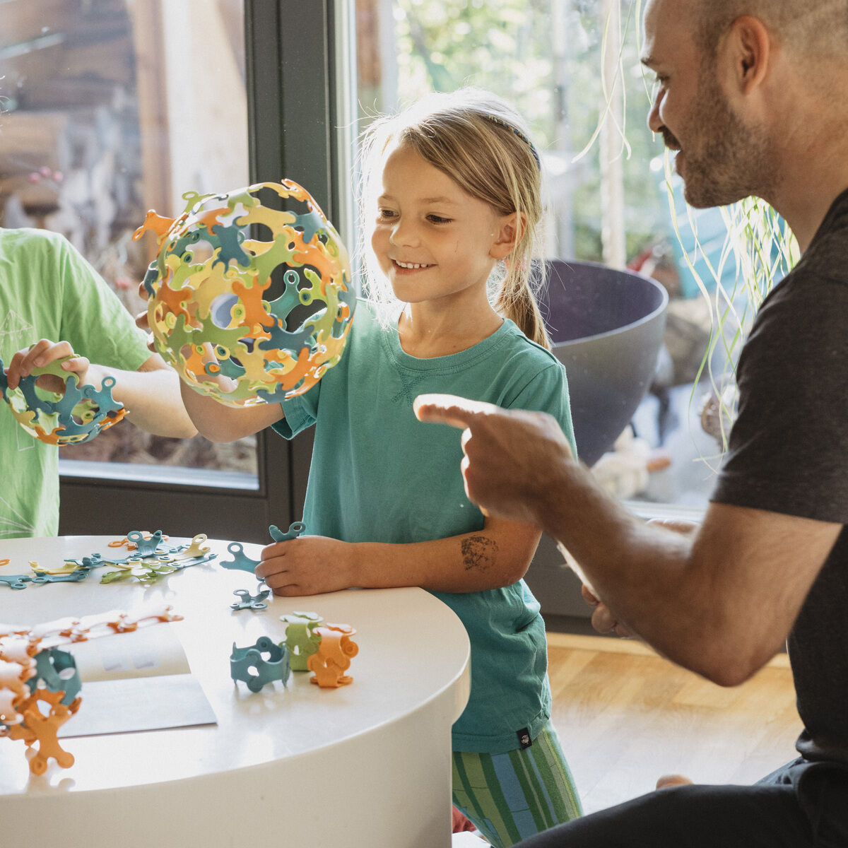 Vier Kinder sitzen an einem runden Tisch und spielen mit Binabo, einem bunten Steckspielzeug bestehend aus verschiedenen Formen und Farben.