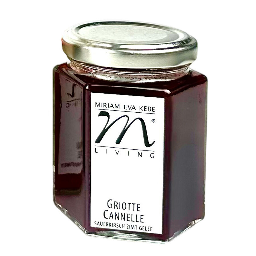 Ein sechseckiges Glas mit silbernem Metalldeckel, gefüllt mit dunkelrotem Sauerkirsch-Zimt-Gelée. Auf dem weißen Etikett stehen die Marke "Miriam Eva Kebe Living" und die Sortenbezeichnung "Griotte Cannelle Sauerkirsch Zimt Gelée". Das Glas ist vor hellem Hintergrund freigestellt.