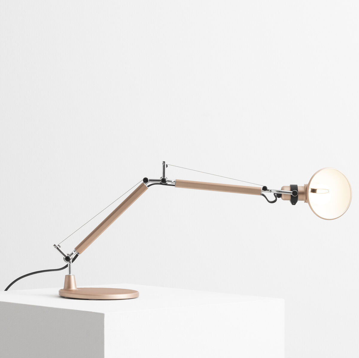 Die Artemide »Tolomeo Micro« ist eine moderne Tischlampe mit einem minimalistischen Design. Die Lampe besteht aus einer verstellbaren Metallstruktur in Holzfarben und Aluminium-Elementen, montiert auf einem weißen Podest.