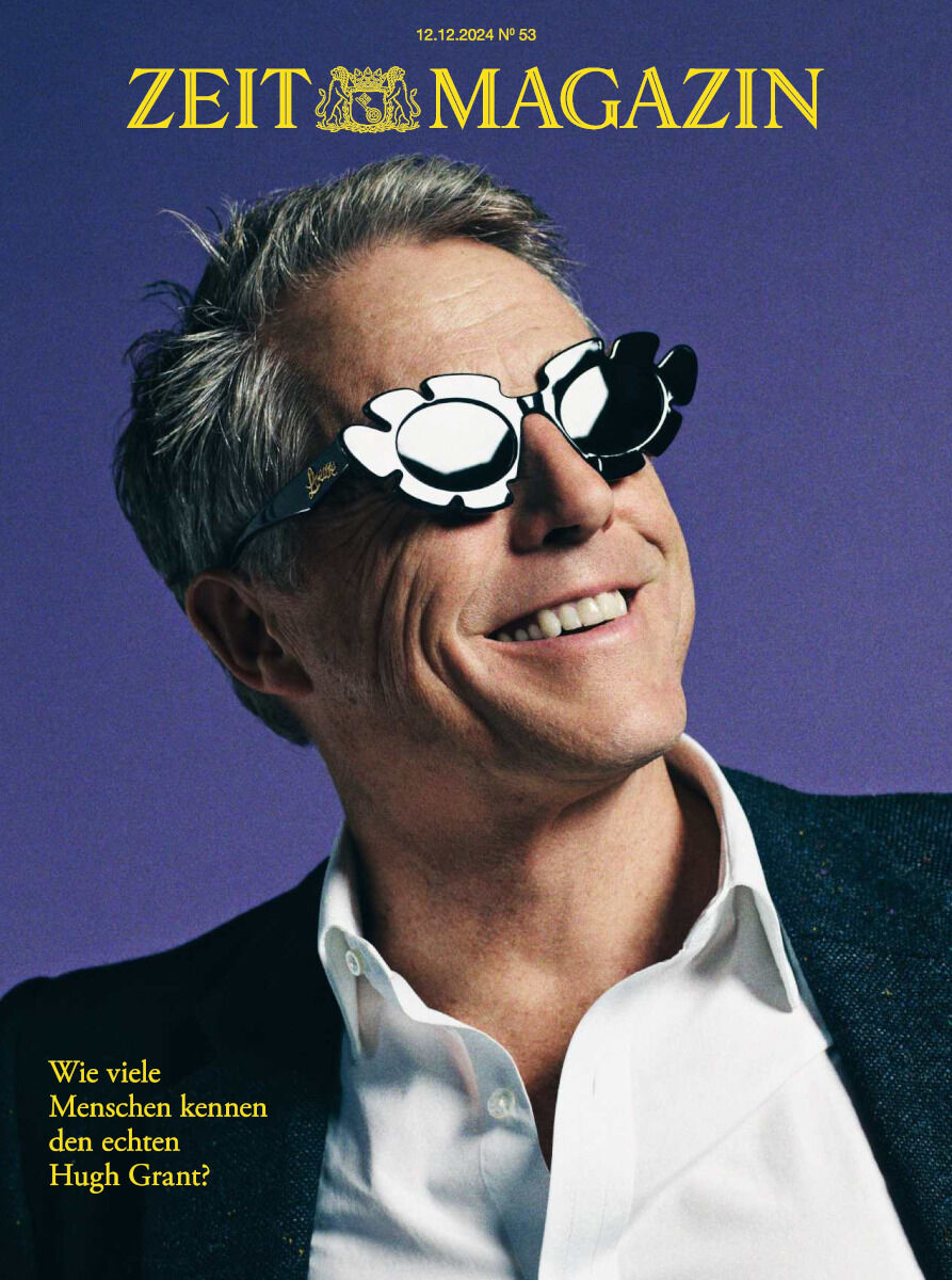 Titelbild des ZEIT Magazins 53/2024 mit einem Porträt von Hugh Grant, der eine Blüte-Sonnenbrille trägt, auf blauem Hintergrund.