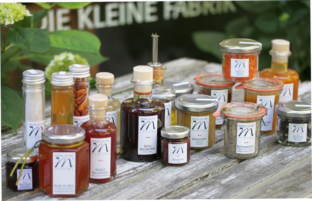 Eine Auswahl an kulinarischen Spezialitäten in Gläsern und Flaschen, schön arrangiert auf einem Tisch im Freien. Enthalten sind verschiedene Saucen, Gewürze und Delikatessen, die handgemacht und liebevoll verpackt sind.