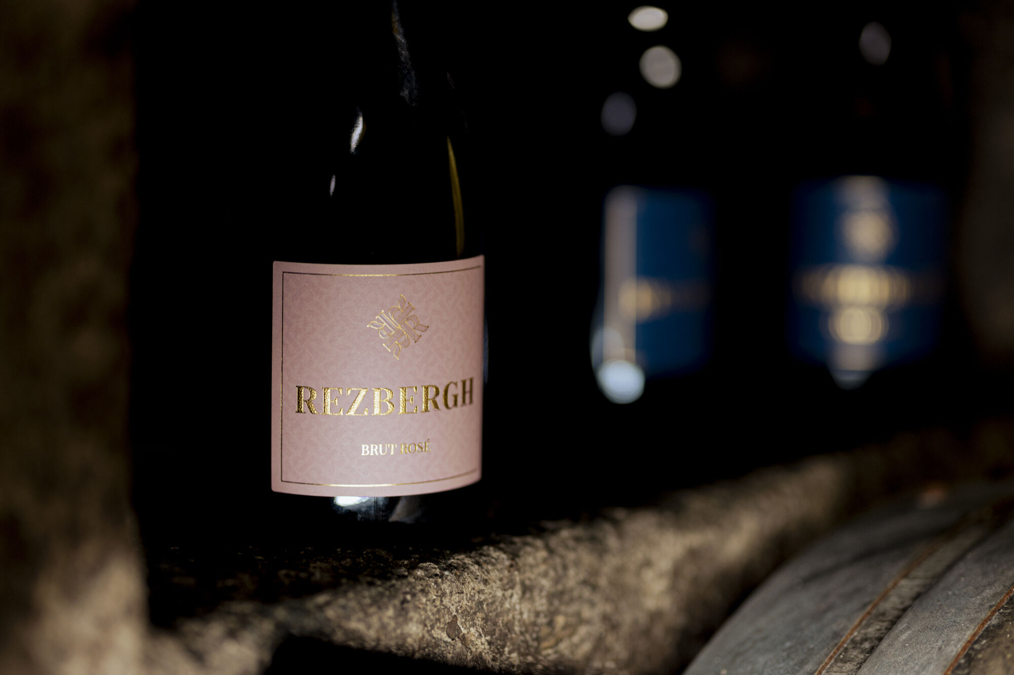 Flasche Rezbergh Brut Rosé mit rosa Etikett in dunklem Weinkeller auf Steinablage