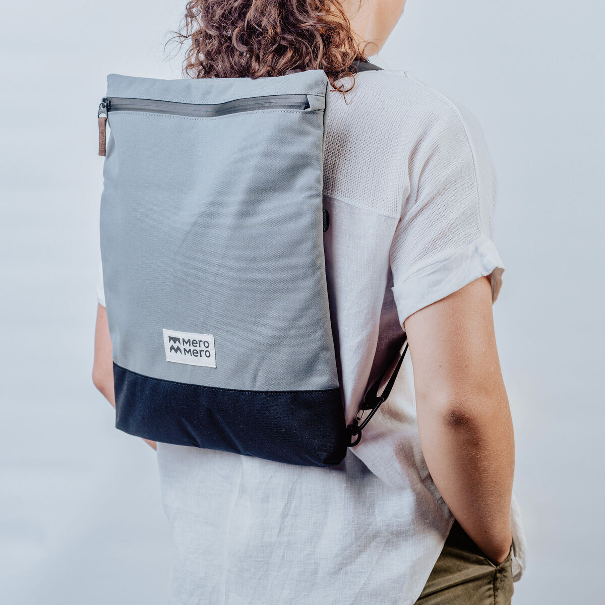 Person trägt grauen und schwarzen Rucksack mit Reißverschluss und Logo »Meije« auf der Rückseite.
