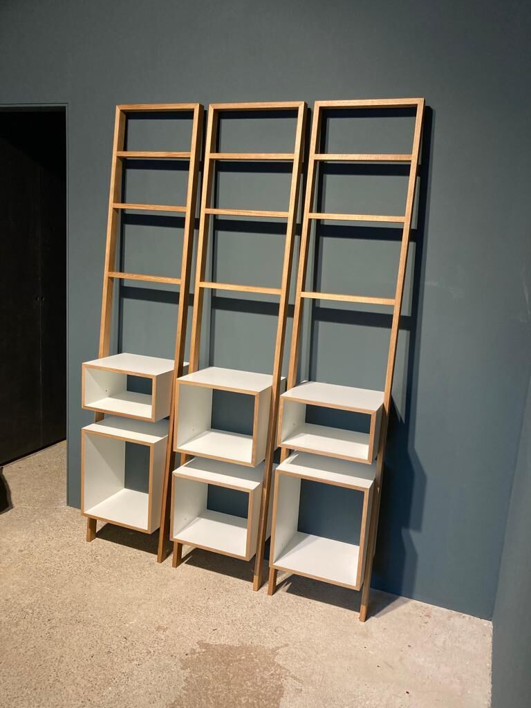 Drei Leitregale aus hellem Holz mit weißen Fächern, die vor einer dunkelgrauen Wand stehen.