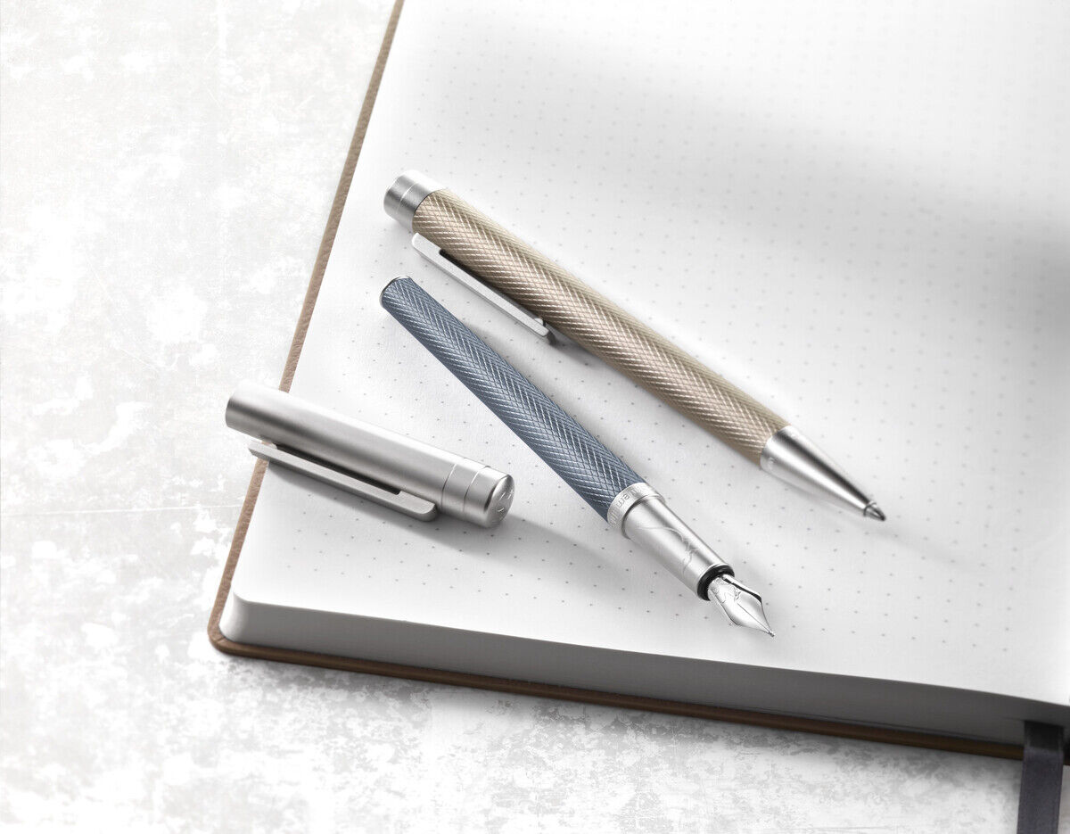 Drei elegante Stifte, darunter ein Rollerball der »Slim Edition«, liegen auf einem aufgeschlagenen Notizbuch. Die Stifte sind in Silber, Blau und Beige gehalten und strahlen eine luxuriöse, moderne Ästhetik aus.