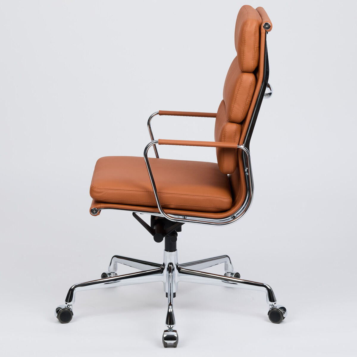 Der Vitra Soft Pad EA219 Schreibtischstuhl in cognacfarbenem Leder ist seitlich vor weißem Hintergrund zu sehen. Er zeigt das elegante, voll verchromte Gestell, weich gepolsterte Sitz- und Rückenfläche sowie die mit Leder ummantelten Armlehnen. Edle, stilvolle Ausstrahlung.