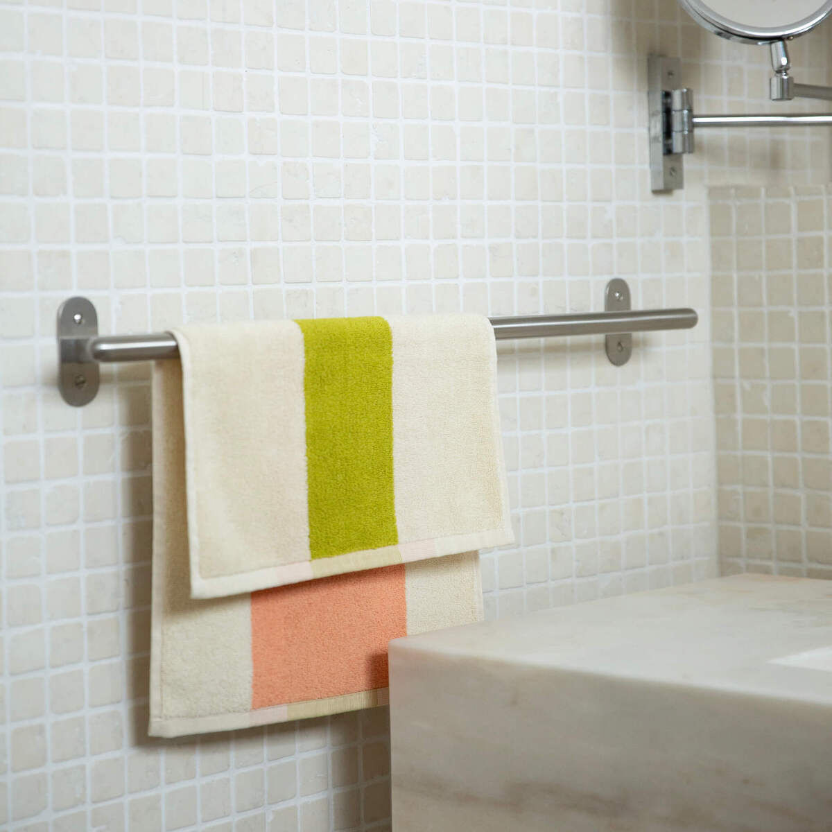 Zwei Gästehandtücher hängen ordnungsgemäß gefaltet auf einer Handtuchstange in einem modernen Badezimmer mit einer weißen, gefliesten Wand und einem Spülbecken.