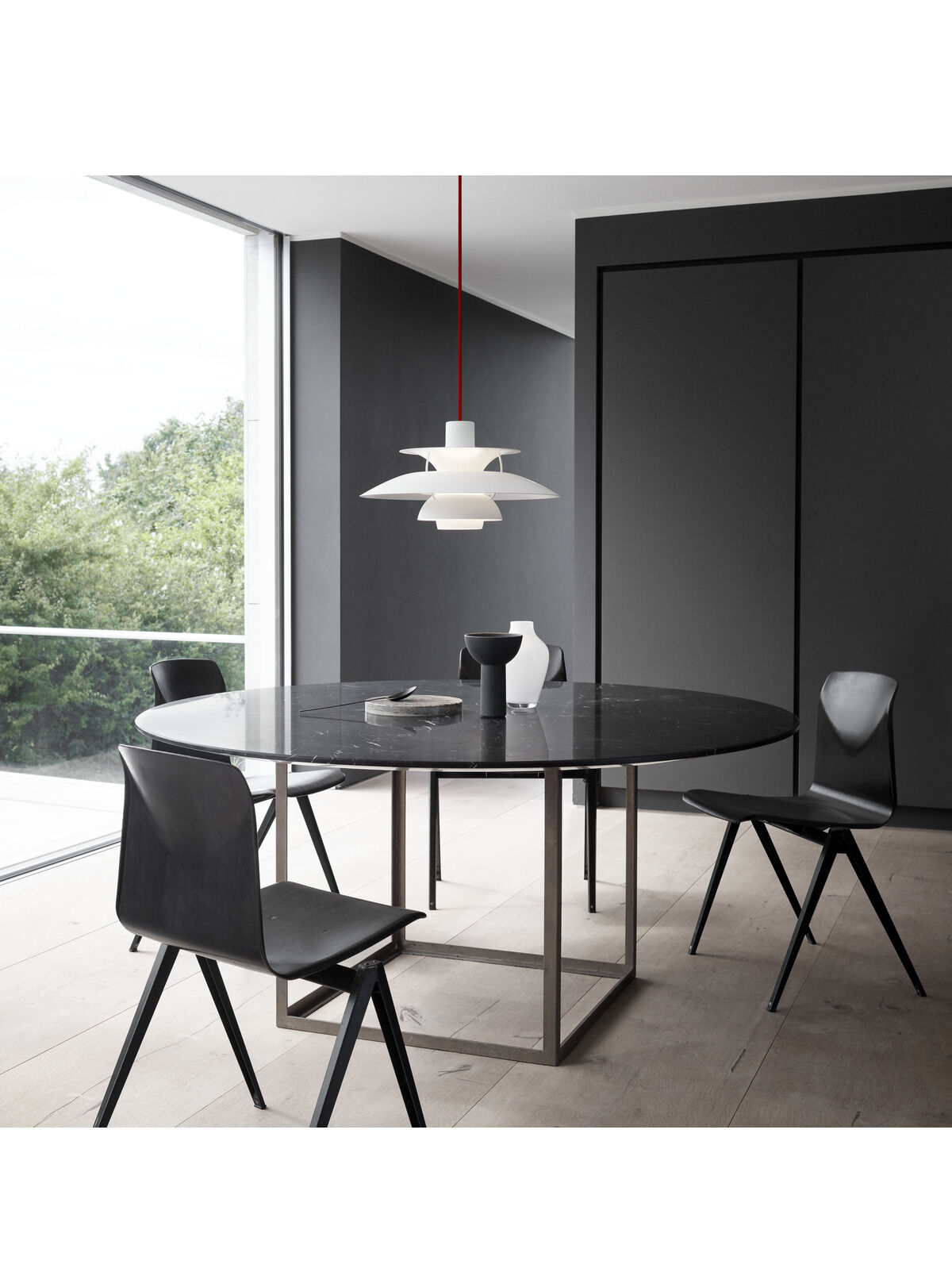 Moderne Pendelleuchte PH5 Monochrome in Weiß und Rot, über einem runden Esstisch in einem eleganten und minimalistischen Esszimmer mit grauen und schwarzen Akzenten.