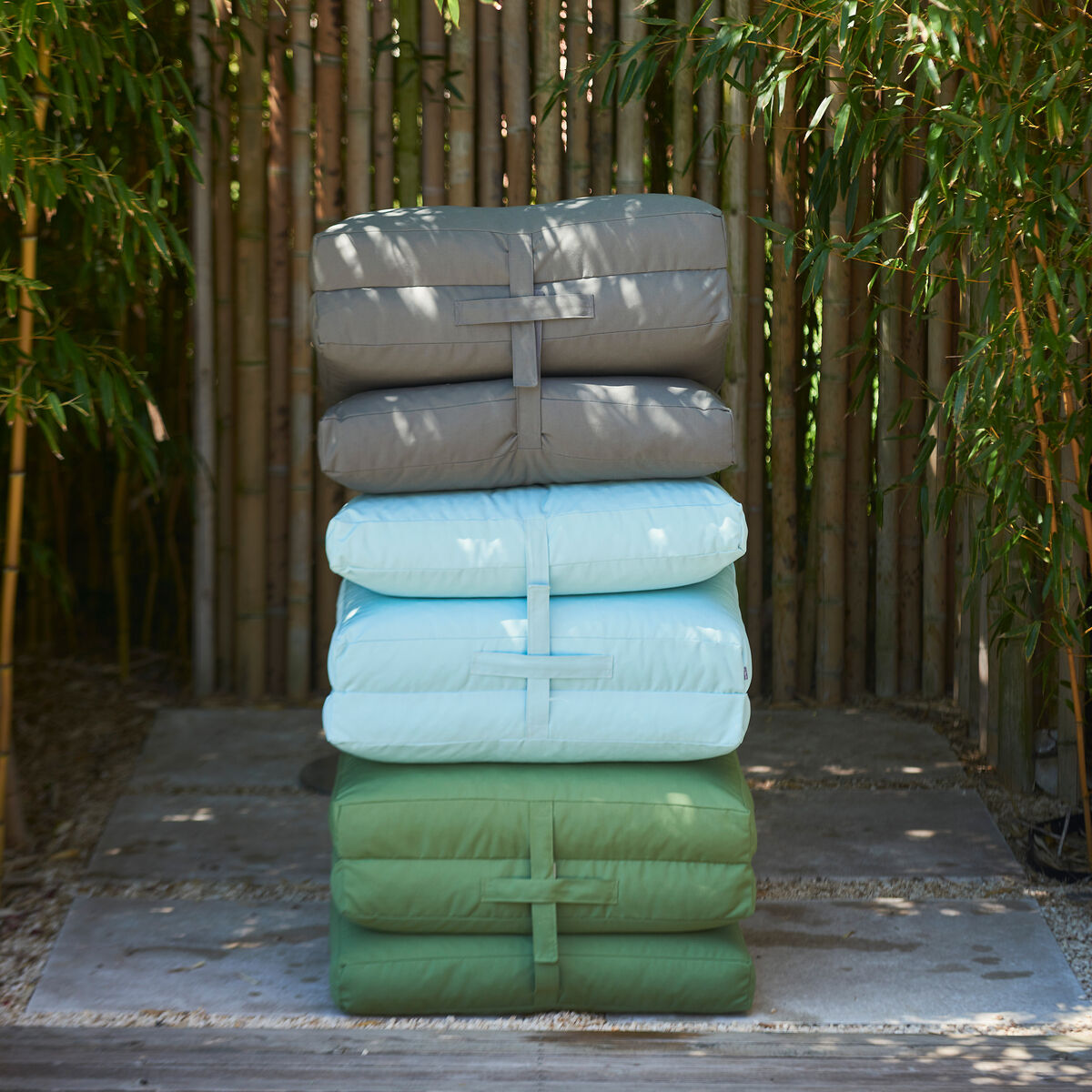 Drei Faltmatratzen der Gartenmatratze »Sheffield« in verschiedenen Farben (Grau, Hellblau, Grün) sind vor einem Bambushintergrund gestapelt.