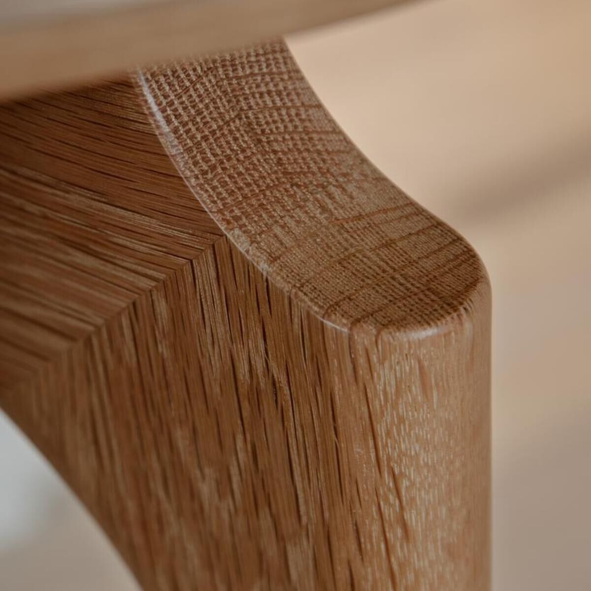 Detailaufnahme eines modernen Schreibtisches aus hellbraunem Massivholz mit glatter, abgerundeter Kante. Das minimalistische Design betont die natürliche Holzmaserung und hochwertige Verarbeitung. Die Szene ist in neutralen, warmen Farbtönen gehalten.