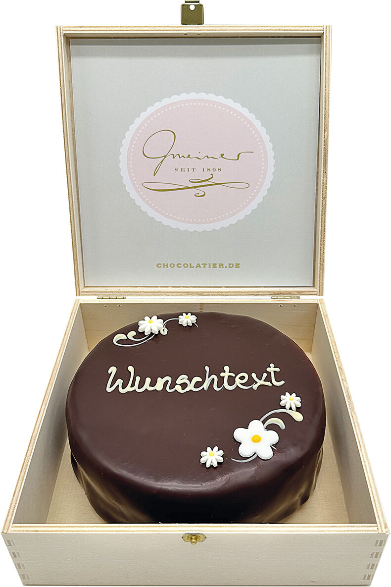 Eine Sachertorte in einer eleganten Box präsentiert, mit einer glatten, glänzenden Schokoladenglasur und dekorativen weißen Blüten sowie einem individuellen Wunschtext.