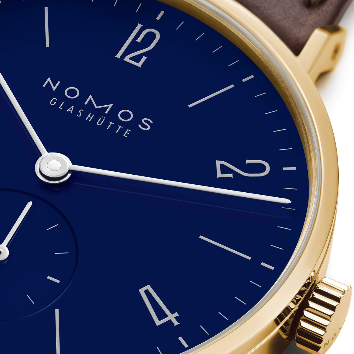 Nahaufnahme einer NOMOS Glashütte Armbanduhr Sonderedition Tangente Gold 33 doré mit emailliertem dunkelblauem Zifferblatt, goldfarbenem Gehäuse und braunem Lederarmband. Die Zeiger und Indizes sind fein gearbeitet, die Uhr wirkt elegant und modern.