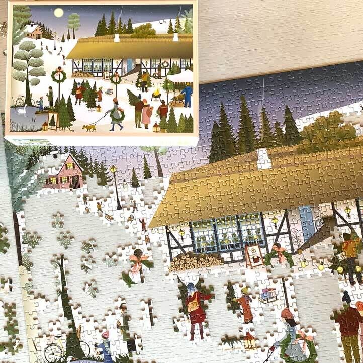 Ein Weihnachtspuzzle mit einer idyllischen Winterlandschaft, die eine verschneite Farm mit Menschen, Tieren und Weihnachtsdekorationen zeigt. Im Bild sind auch ein fertiggestelltes Puzzle und eine Tasse Tee zu sehen.