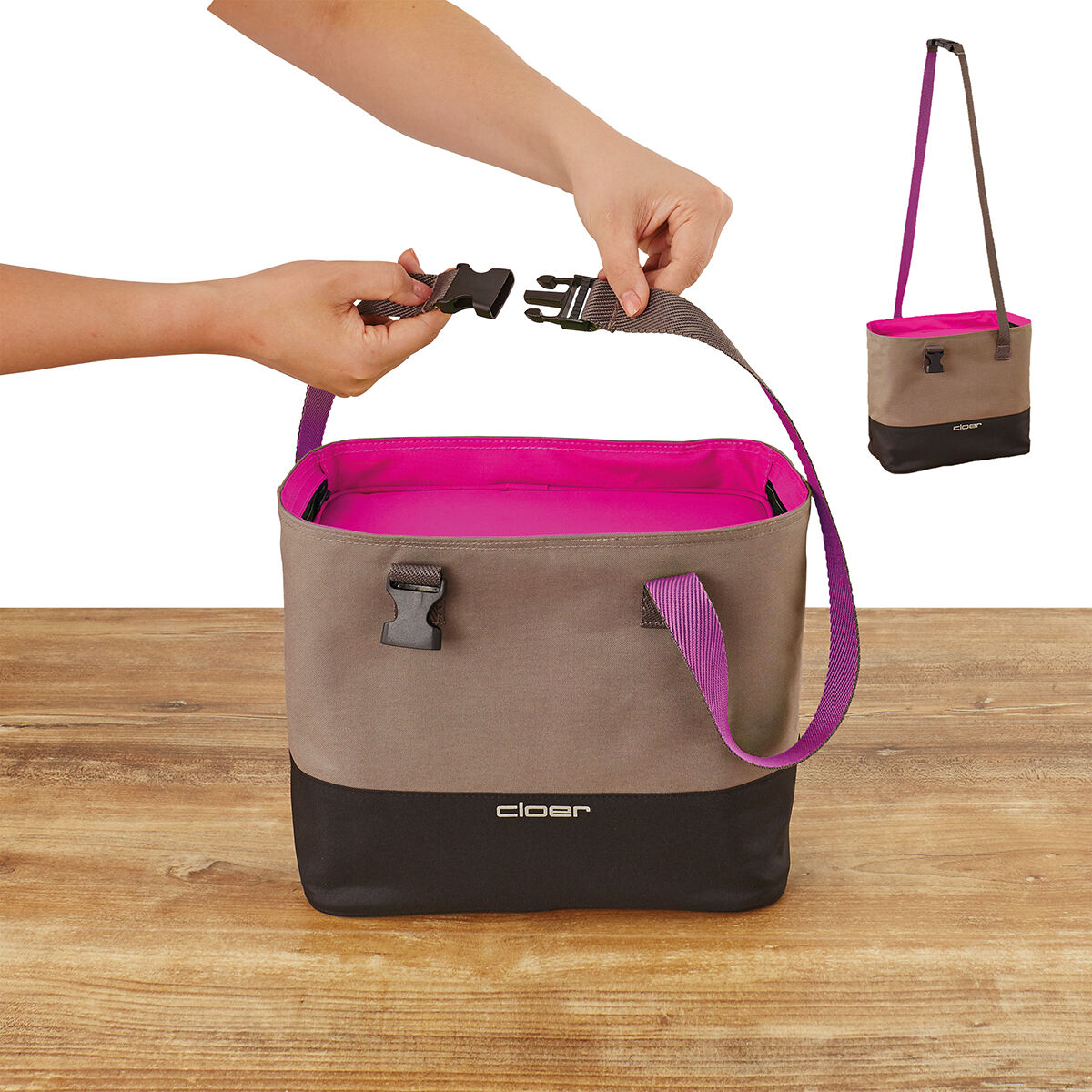 Eine Lunch-Tasche mit beigen Außenflächen, pinkem Innenfutter und schwarzem Boden. Sie hat einen lila Tragegurt und eine schwarze Schnalle. Die Tasche wird von zwei Händen gehalten, eine öffnet eine der Schnallen. Im Hintergrund ist die gleiche Tasche nochmals abgebildet, dieses Mal hängend.