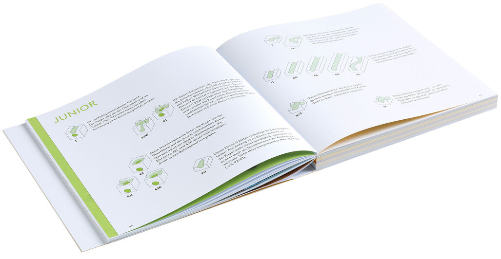 Das Bild zeigt ein aufgeschlagenes Buch mit Anleitungen und Illustrationen zur Konstruktion einer Kugelbahn des Produkts »Cuboro - Das Buch«. Die Seiten sind in Weiß mit grünen und gelben Akzenten gestaltet.