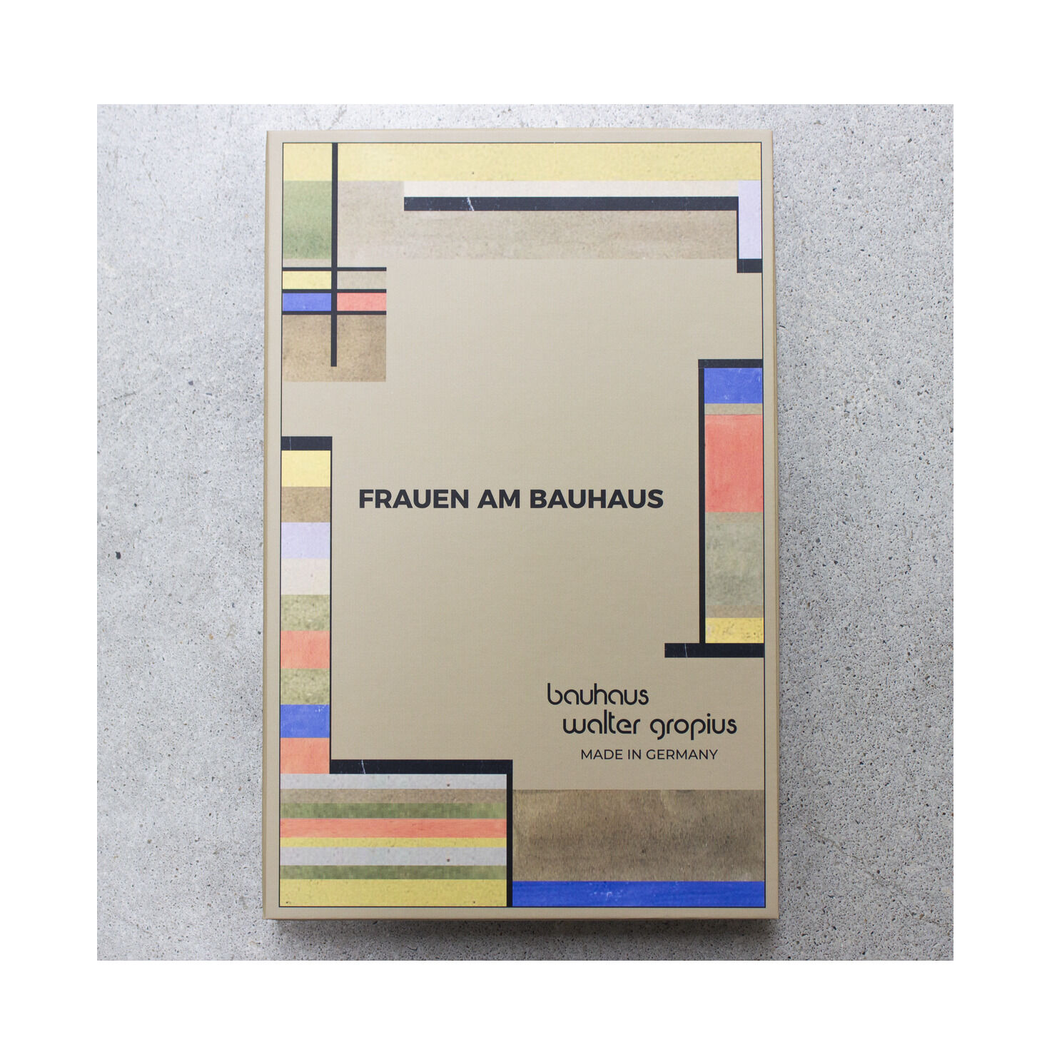 Rechteckige Verpackung mit moderner, geometrischer Gestaltung im Bauhaus-Stil: Streifen und Rechtecke in Beige, Schwarz, Blau, Rot, Grün, Gelb und Rosa. Zentral der Schriftzug „Frauen am Bauhaus“. Darunter Herstellerangaben: bauhaus, Walter Gropius, Made in Germany.