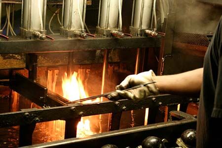 Hand mit Handschuh hält Metallrahmen über offene Flamme in industrieller Umgebung