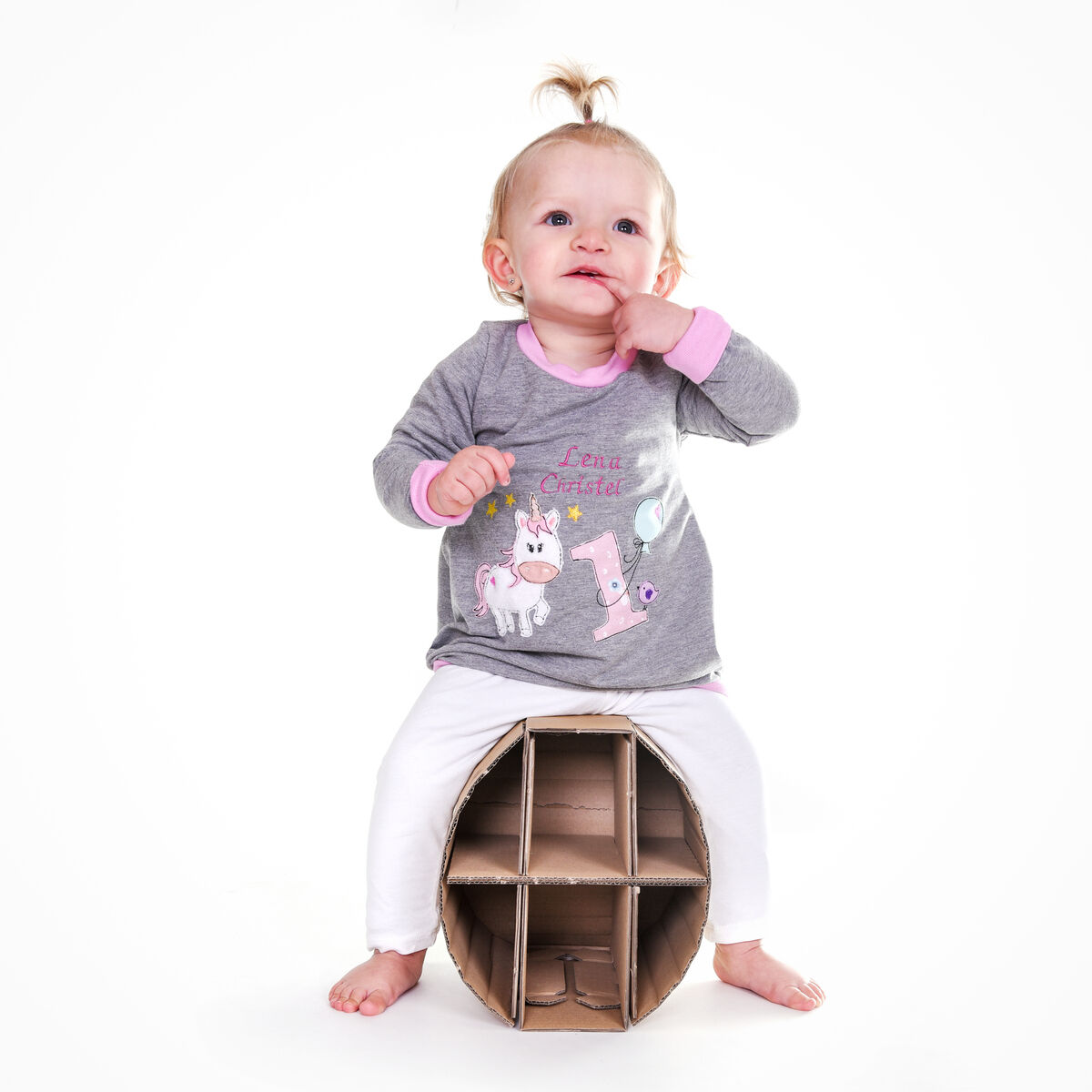 Ein kleines Kind sitzt auf dem Papphocker »Lollo«. Der Hocker besteht aus braunem Karton und hat eine stabile, durchdachte Konstruktion. Das Kind trägt einen grauen Pullover und weiße Hosen.