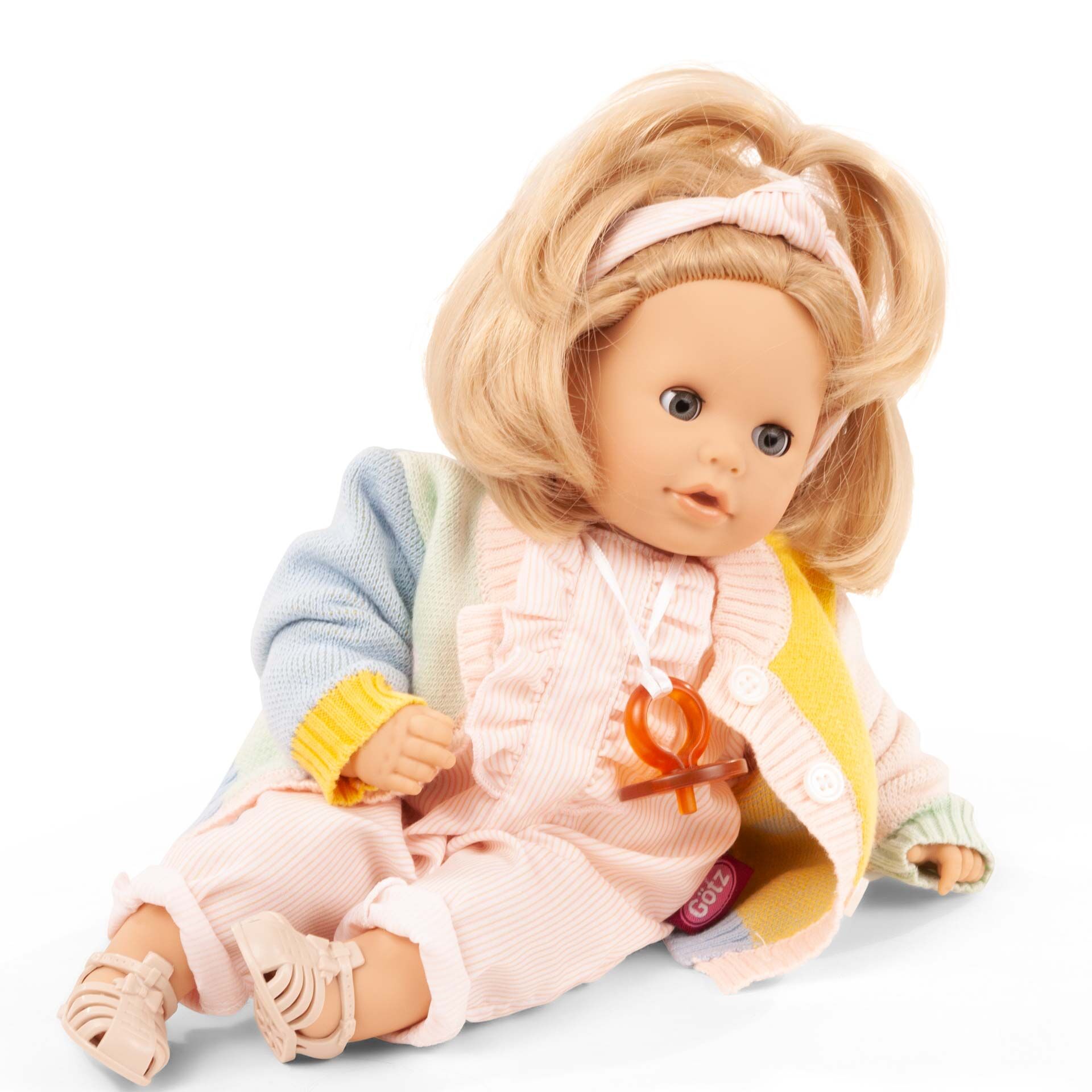 Sitzende Badepuppe »Cosy Aquini Farbspiel« mit blonden Haaren, bekleidet mit einem rosa Strampler, gemusterter bunter Strickjacke sowie Stirnband und weißem Schnuller, geeignet als Kinderspielzeug und Geschenk.