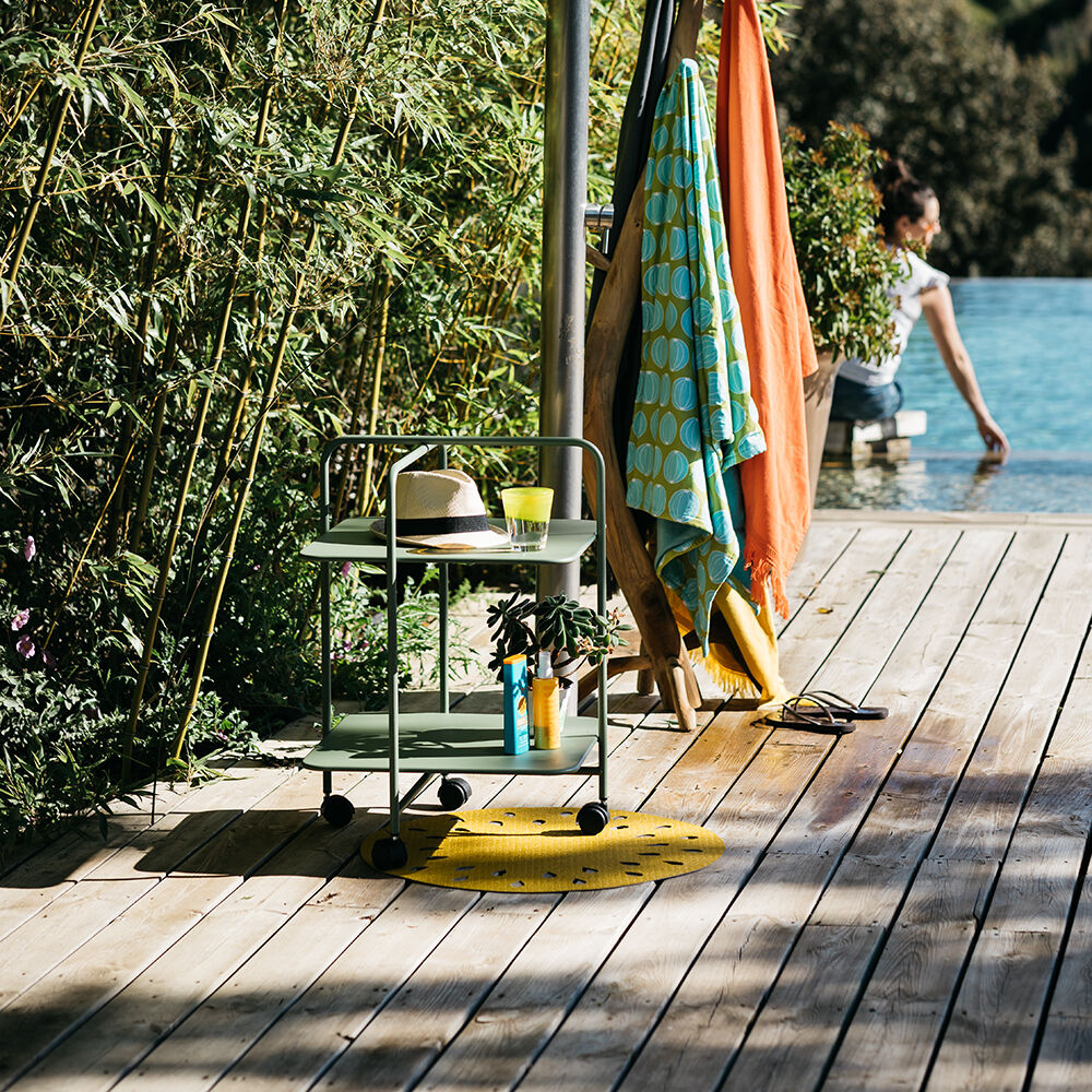 Beistelltisch 'Alfred' im Freien neben einem Pool, umgeben von Bambus, mit einem Sonnenhut und Getränken darauf.