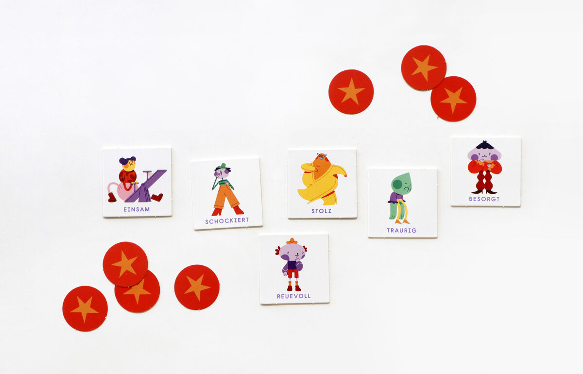 Spiel 'Bingo der Emotionen' mit sechs Karten, die verschiedene Emotionen darstellen, und mehreren roten Spielmarken mit Sternen darauf. Jede Karte zeigt eine farbige Illustration einer Figur, die eine bestimmte Emotion ausdrückt, z.B. einsam, schockiert, stolz, traurig, besorgt, reuevoll.