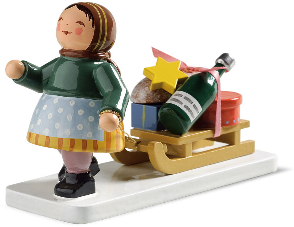 Detaillierte Holz-Figur von Wendt & Kühn: Ein Mädchen mit grünem Oberteil, hellblauem Rock mit weißen Punkten und Kopftuch zieht einen gelben Schlitten mit Geschenken, Flasche, Stern und Deko auf weißem Sockel. Ideal als Winter- oder Weihnachtsdeko.