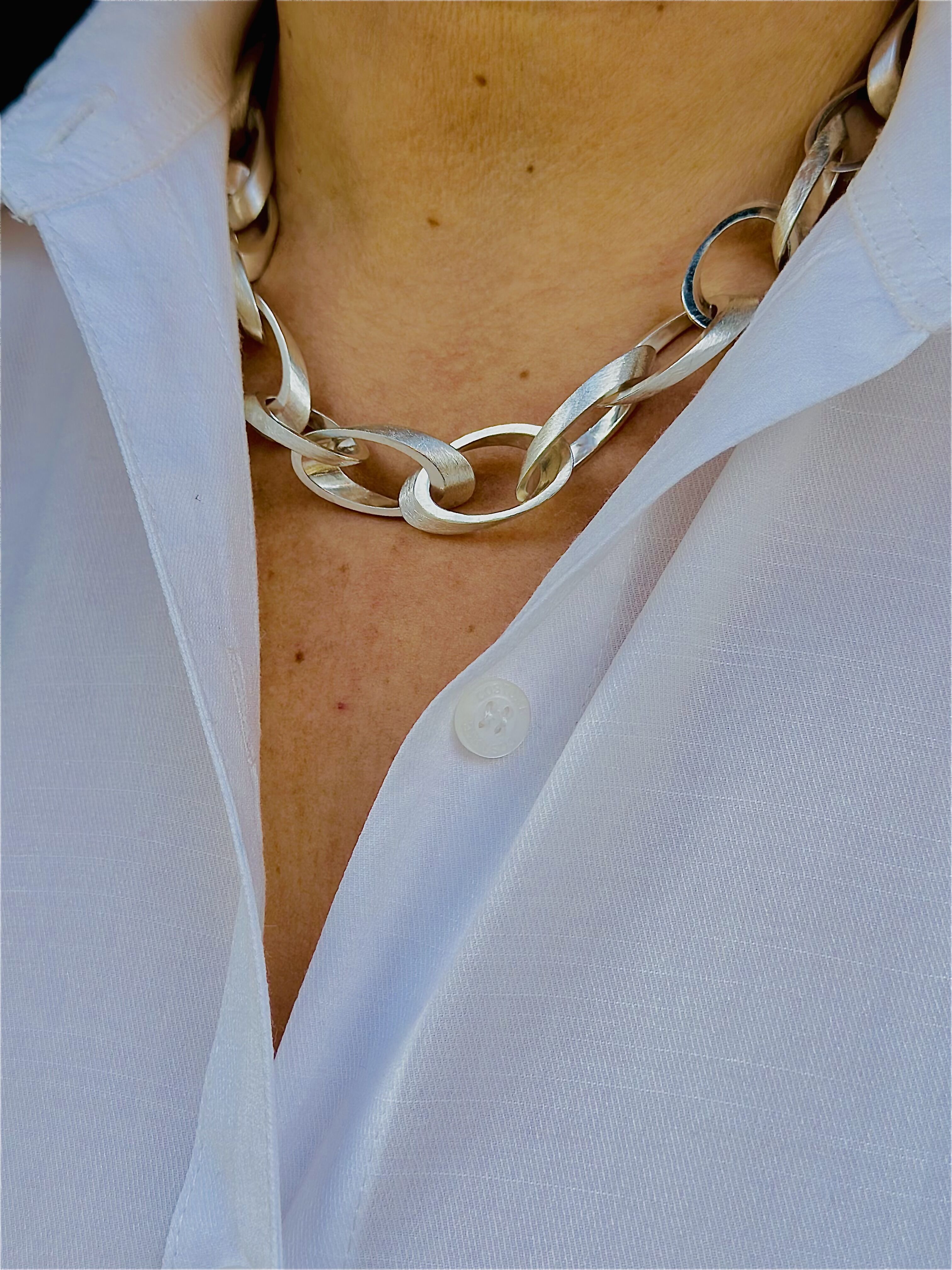 Nahaufnahme eines silbernen Colliers namens 'Jackie', getragen über einem weißen Hemd, das die Eleganz und den klassischen Stil des Schmucks hervorhebt.