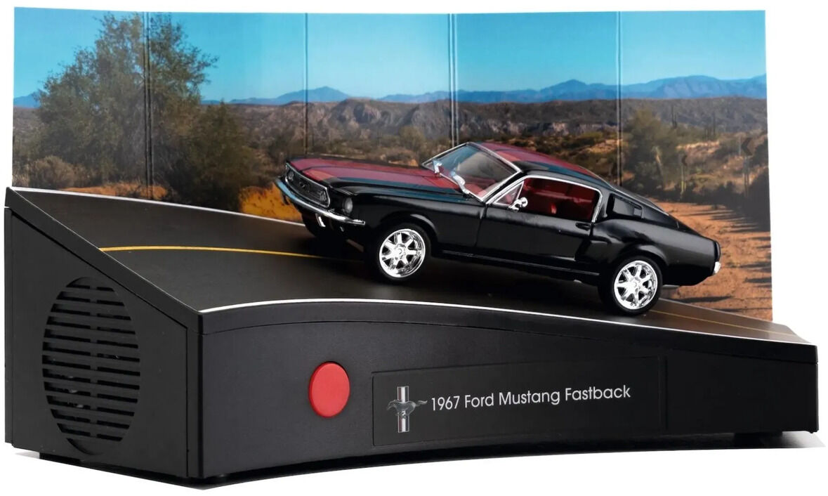 Schwarzes Modell eines Ford Mustang Fastback von 1967 mit roten Streifen und silbernen Custom-Felgen auf einer schwarzen Soundbasis. Vorn sind ein roter Knopf und die Aufschrift „1967 Ford Mustang Fastback“, links ein Lautsprechergitter. Dahinter steht eine dreiteilige Wüstenlandschaft-Kulisse.