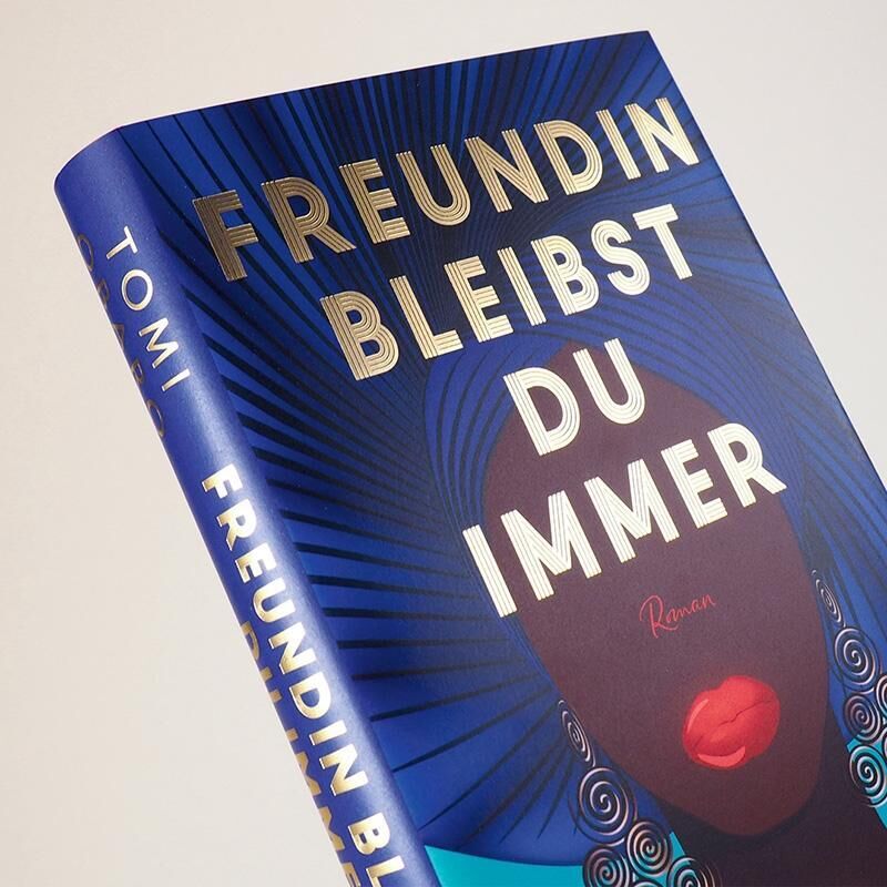 Das Bild zeigt das Buch 'Freundin bleibst du immer' von Tomi Obaro. Das Cover ist hauptsächlich blau mit goldener Schrift und zeigt eine stilisierte Illustration eines roten Lippenstifts. Es ist ein Roman über Freundschaft, ideal als Geschenk für Leserinnen und Jugendliche.