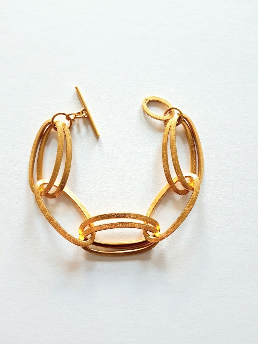 Ein elegantes, goldenes Armband bestehend aus miteinander verbundenen ovalen Gliedern mit einem T-Verschluss, das auf einem weißen Hintergrund fotografiert wurde.