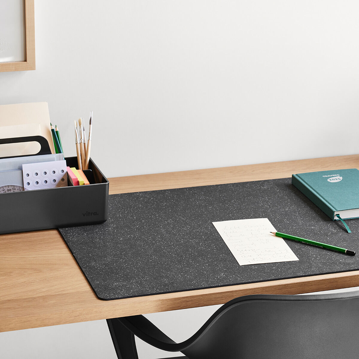 Ein minimalistischer Schreibtisch mit einer praktischen Toolbox zum Organisieren von Stiften, Dokumenten und anderem Büromaterial. Ein Notizbuch und ein Stift liegen auf einer schwarzen Schreibtischunterlage.