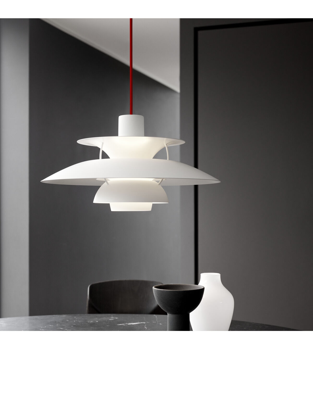 Moderne Pendelleuchte mit weißem und rotem Design, hängt über einem Marmortisch mit dekorativen Objekten. Die monochrome Leuchte hat eine elegante, zeitlose Form, perfekt für skandinavische Inneneinrichtung.