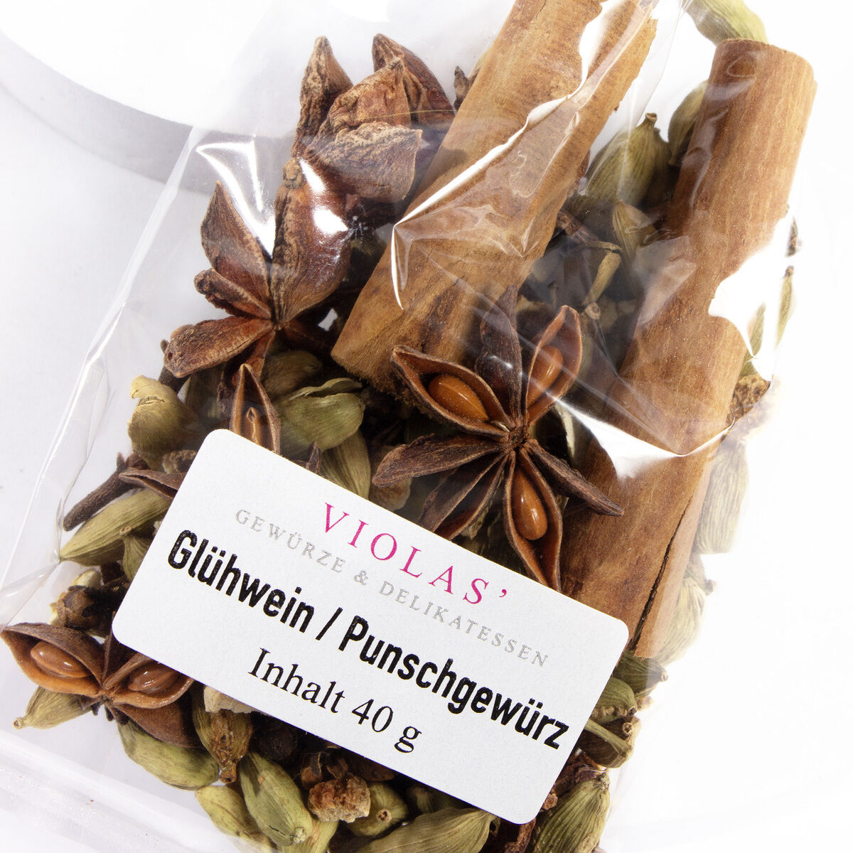 Ein naher Blick auf eine Tüte mit Glühwein- und Punschgewürzen, einschließlich Sternanis, Zimtstangen und Kardamom, beschriftet mit 'VIOLAS' Glühwein / Punschgewürz, Inhalt 40 g.