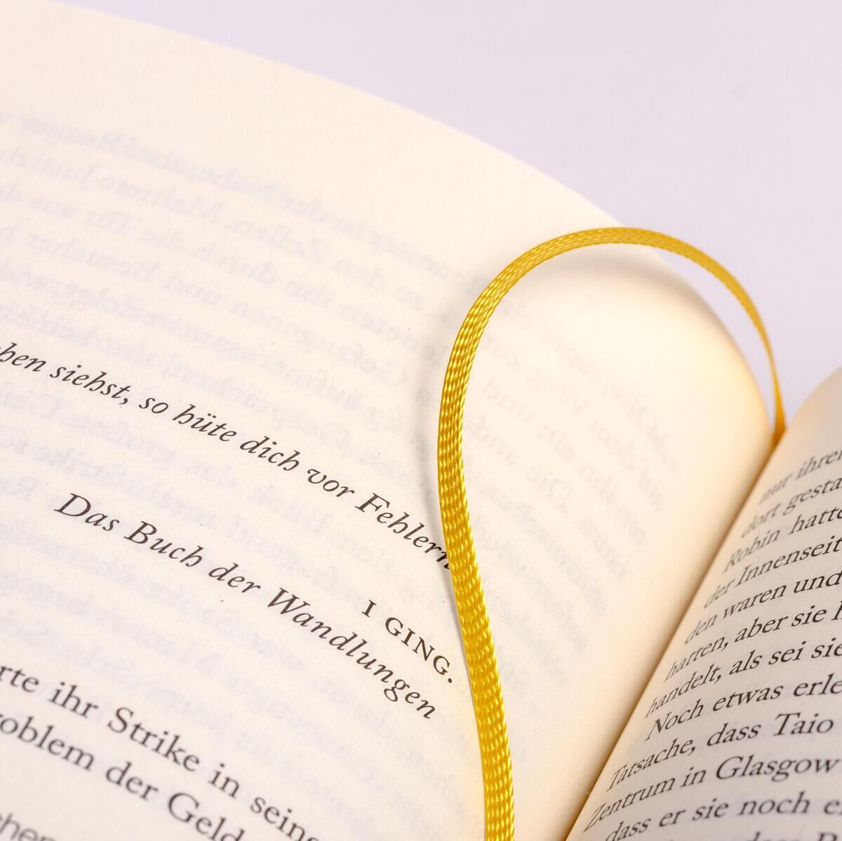 Nahaufnahme eines aufgeschlagenen Buches mit einem gelben Lesezeichen, das zwischen den Seiten liegt. Der Fokus liegt auf den gedruckten Wörtern der Buchseiten.