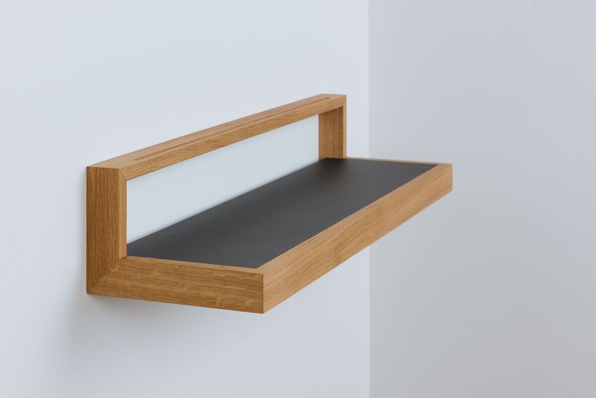 Ein schwebendes Wandregal mit einem Holzrahmen und einer anthrazitfarbenen Ablagefläche. Die Rückwand ist weiß.