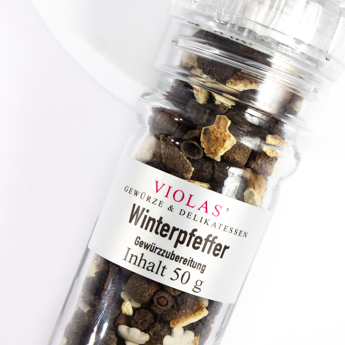 Ein Gewürzstreuer mit der Aufschrift 'VIOLAS' Gewürze & Delikatessen: Winterpfeffer Gewürzubereitung' gefüllt mit einer Mischung aus verschiedenen Gewürzen auf einem weißen Hintergrund.